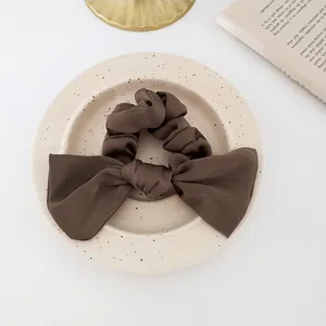 Detailed close-up of a dark coffee satin oversized bow scrunchie on a decorative tray