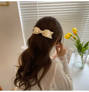Detail of elegant cream satin bow hair clip styled on hair with a smooth silk texture