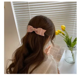 Detail view of a pale pink satin bow hair clip styled on wavy brunette hair