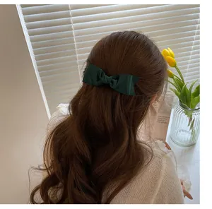 Elegant dark green satin bow hair clip styled on wavy hair for a classic French look