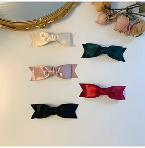 Flat lay of five satin bow hair clips in cream, green, pink, red, and black colors