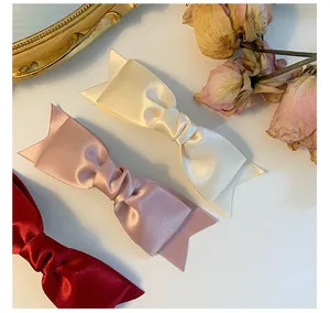 Detailed close-up of French satin bow hair clips in cream, pink, and burgundy silk colors