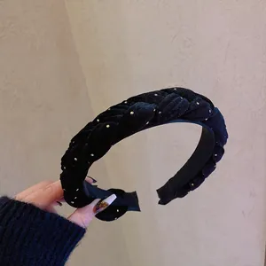Braided black velvet headband with gold metal studs held against a beige background