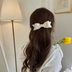 Elegant cream satin bow hair clip styled on wavy brown hair for a French aesthetic look