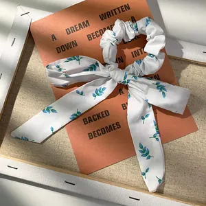 Detail eines floralen Scrunchies mit Bändern und blaugrünem Blattdruck auf weißer Seide