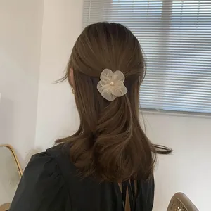 Close-up of elegant apricot organza flower hair clip with pearl on brown wavy hair