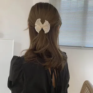 Detailed back view of apricot tulle bow hair clip with pearls on long wavy hair
