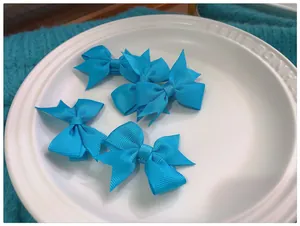 Détail de cinq pinces à cheveux à nœuds en ruban gros-grain bleu clair sur une assiette blanche