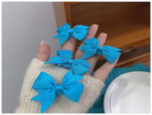 Détail de quatre barrettes à cheveux avec nœuds en ruban bleu lac tenues dans la main