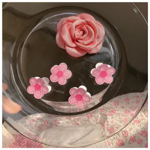 Close-up of pink fabric rose and small floral hairpins displayed on a glass tray