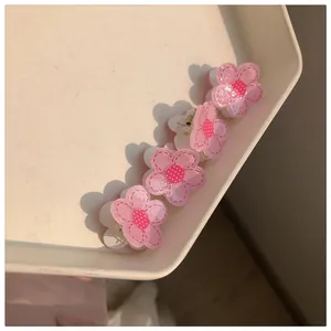 Detail of four pink camellia flower hair clips with glitter finish on a beige tray