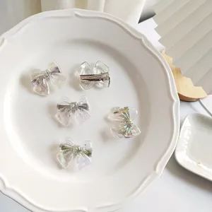 Close-up of five iridescent bow hair clips in a white ceramic dish with soft lighting