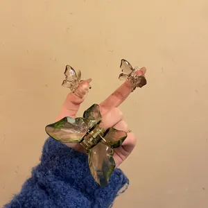 Hand holding a set of translucent butterfly hair claws in olive green and brown tones