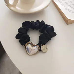 Chouchou en satin noir avec pendentif cœur irisé et breloque dorée sur un bureau