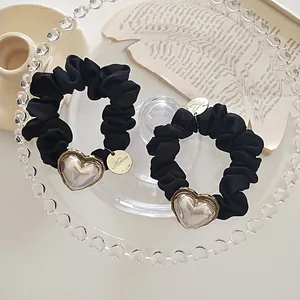 Détail de chouchous en satin noir avec breloques cœur miroir et accents en métal doré