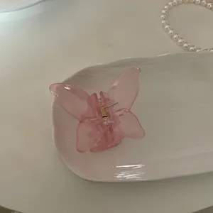 Pinza per capelli a farfalla rosa traslucida con molla dorata su vassoio in ceramica