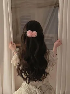 Détail d'une pince à cheveux camélia rose posée sur de longs cheveux ondulés sombres