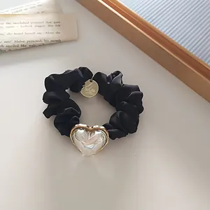 Détail d'un chouchou en soie noire avec un cœur iridescent et un pendentif doré