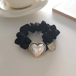 Détail d'un chouchou en velours noir avec un pendentif cœur perlé et un charme doré chic