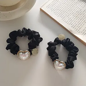 Vue détaillée de chouchous en satin noir avec breloques cœur perlé et médaillon doré