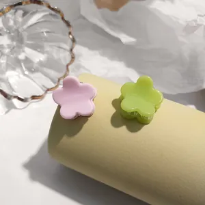 Chic cream-colored mini flower hair claws in pink and green on a yellow display stand