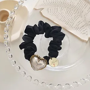 Détail d'un chouchou en soie noire avec pendentif cœur transparent et breloque dorée