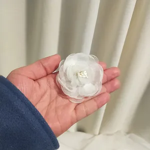 Detailed view of layered white chiffon camellia flower hair clip held by hand