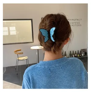 Blue butterfly hair claw clip with black outlines worn by a model in a cafe setting