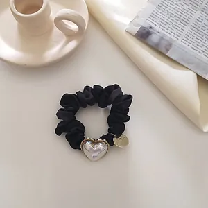 Détail d'un chouchou en satin noir avec un pendentif en cœur et médaillon argenté