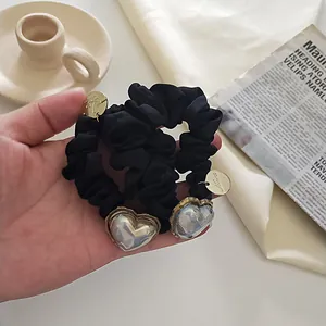 Détail d'un chouchou en soie noire avec pendentif cœur iridescent et breloque dorée