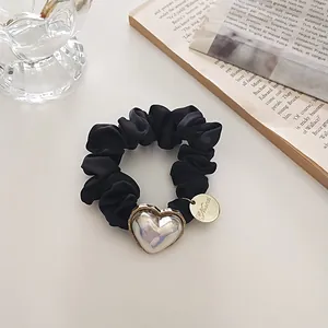 Détail d'un chouchou en satin noir avec pendentif cœur iridescent et étiquette dorée