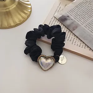 Détail d'un chouchou en satin noir avec cœur perlé irisé et pendentif doré