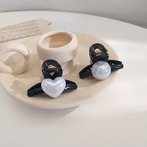Set of two small pearl hair clips with heart and round charms on a cream tray