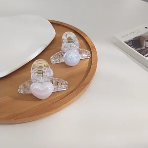 Set of two luxury iridescent pearl hair claws with heart and round charms on a wooden tray