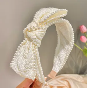 Detailed close-up of cream bow headband with pleated fabric and delicate white pearl trim