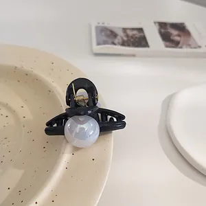 Detail of a minimalist black resin hair claw with a large iridescent white pearl accent