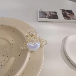 Detailed view of a small heart-shaped pearl acrylic hair claw clip with golden metal spring