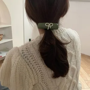 Detail of a dark green rectangular hair clip with a white 3D bow on long brown hair