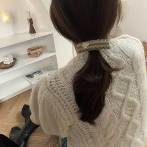 Detail of a khaki wavy ribbon hair clip with a white camellia flower on a model