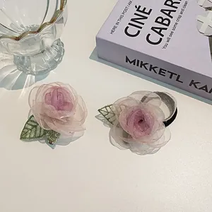 Détail de la pince à cheveux camélia et de l'élastique en maille rose sur table blanche