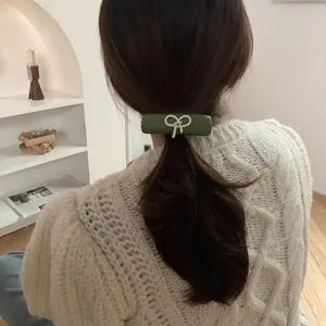 Detail of dark green matte barrette with ivory bow relief on model's low ponytail