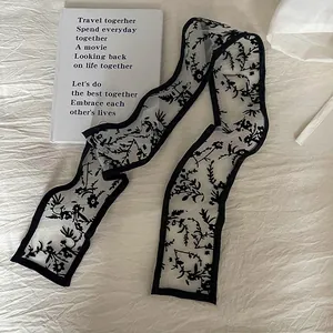 Close-up of semi-transparent lace scarf with black floral patterns and thin black edging