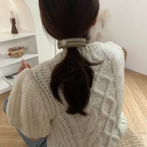 Detail of an olive green woven hair clip with white camellia flower on a ponytail