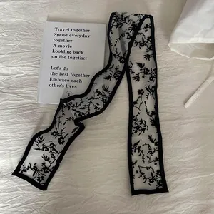 Close-up of black floral lace ribbon scarf with delicate embroidery on white fabric