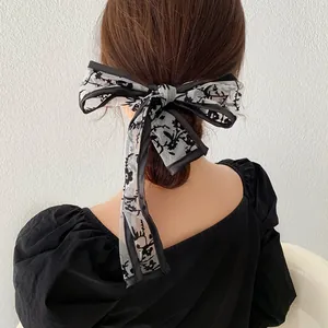 Elegant black lace bow hair scarf with floral patterns shown on a low bun hairstyle
