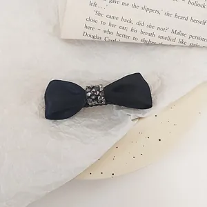 Close-up of a black satin bow hair clip with sparkling rhinestone center on white paper