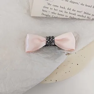 Detail of pink satin bow hair clip with dark rhinestone center and metal clip