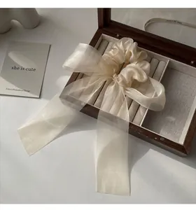 Detailed texture of beige organza hair scrunchie with elegant bow on a wooden box