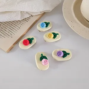 Detailed set of five colorful matte rose hair clips with green leaves on a book