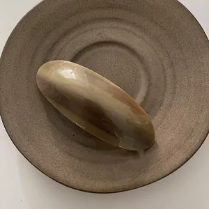 Detalle macro del clip de pelo ovalado ámbar con grabado La France en cuenco cerámico